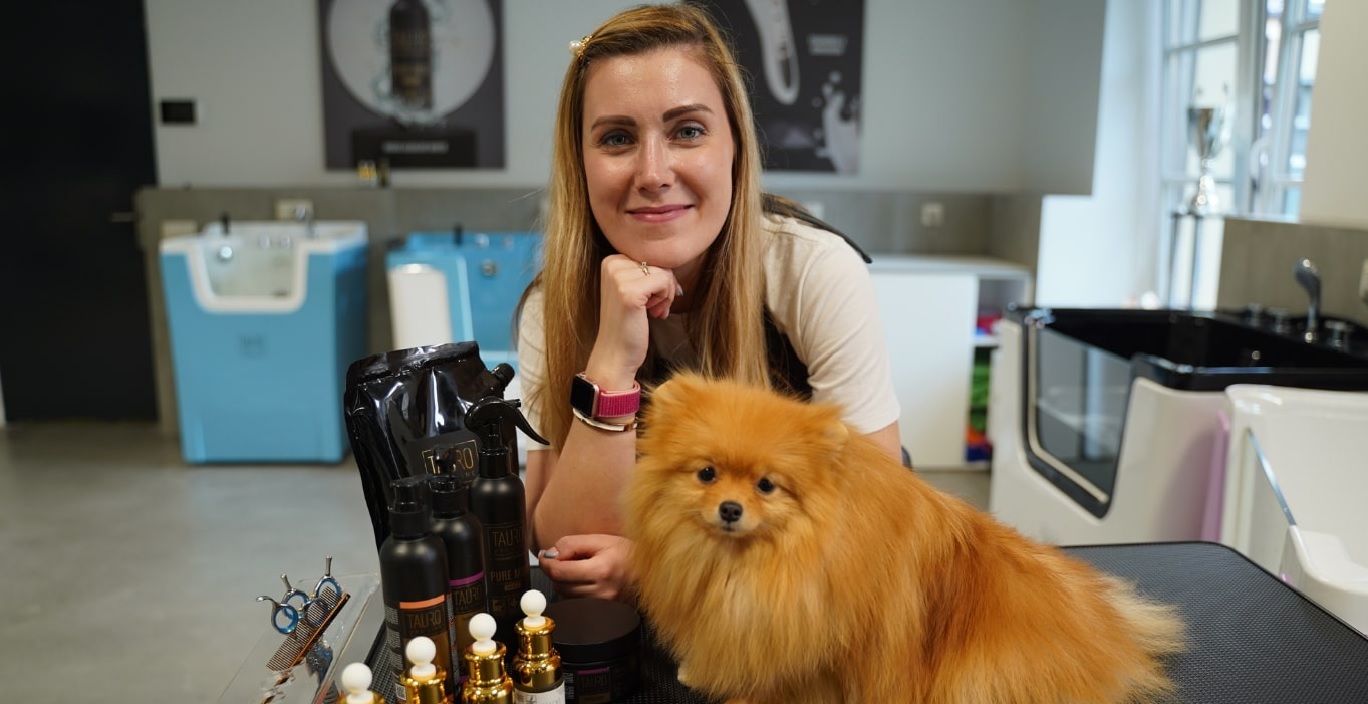 Gyvūnų priežiūros specialistė, šalia jos pomeranijos špicų veislės šuo ir įvairios kosmetinės Tauro pro line priemonės